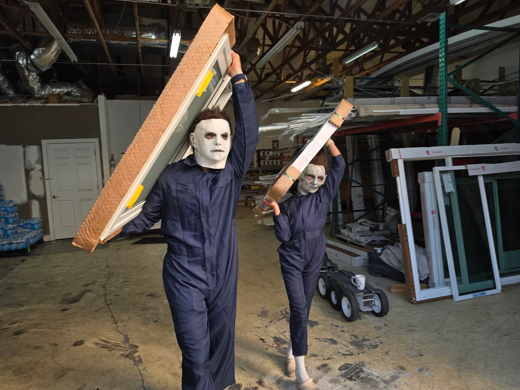 Two costumed O'Donnell team members carrying packaged windows in the warehouse.